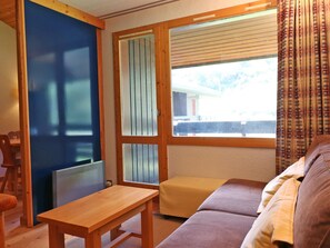 Una habitación con una mesa de madera, un sofá, una ventana con persianas y una puerta con panel de vidrio satinado.