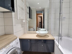 Ein modernes Badezimmer mit einer großen Badewanne, einem Waschbecken mit Schale, einer Waschmaschine und einem Spiegel.