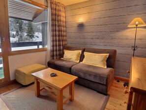Una habitación acogedora con un sofá marrón, una pequeña mesa de madera, una lámpara y vistas a un paisaje nevado a través de la ventana.