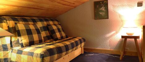 Une chambre mansardée chaleureuse avec un lit superposé en bois, une petite table avec une lampe et un tableau encadré au mur.