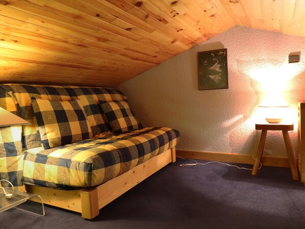 A cozy attic bedroom with a wooden bunk bed, a small table with a lamp, and a framed picture on the wall.