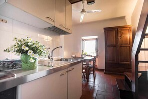 A kitchen with a central island, a sink, and a dining area with wooden chairs. - Turquoise-colored apartment in the historic center with a view of the Umbrian valley (Spello)