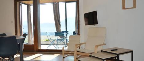 A room with a bed, a desk, and a chair. There is a TV on the wall and a window with curtains.