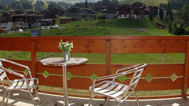 Un balcón con una mesa y dos sillas, con vistas a un pueblo de casas tradicionales y montañas al fondo.