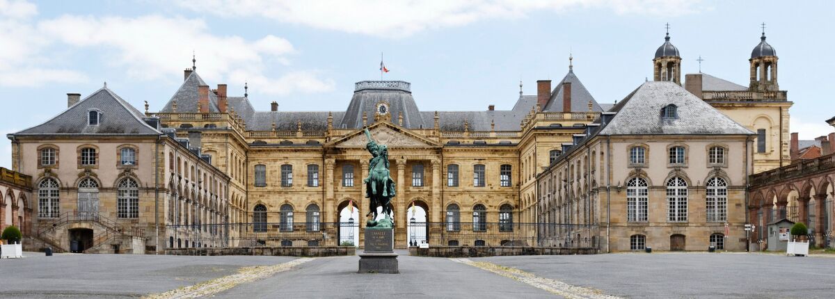 A large historic building with a central statue, symmetrical architecture, and a wide courtyard.