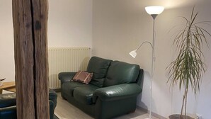 A living room with a green leather sofa, a floor lamp, a potted plant, and a wooden post. - 3-bedroom/two-bathroom house in the countryside (Bezange-la-Grande)