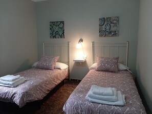 Une chambre avec deux lits, chacun agrémenté d’une couvre-lit et de coussins à motifs, une table de chevet avec une lampe, et deux œuvres d’art accrochées au mur.