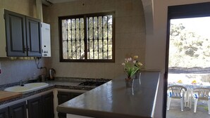 Una cucina con piano di lavoro in granito, lavello, pensili, una finestra con inferriate e una pianta in vaso.