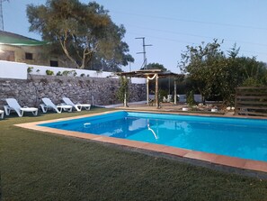 Une piscine rectangulaire avec un mur en pierre et une pergola en arrière-plan.