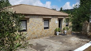 Un edificio in pietra con tetto in tegole, due finestre con inferriate e piante in vaso nel cortile.