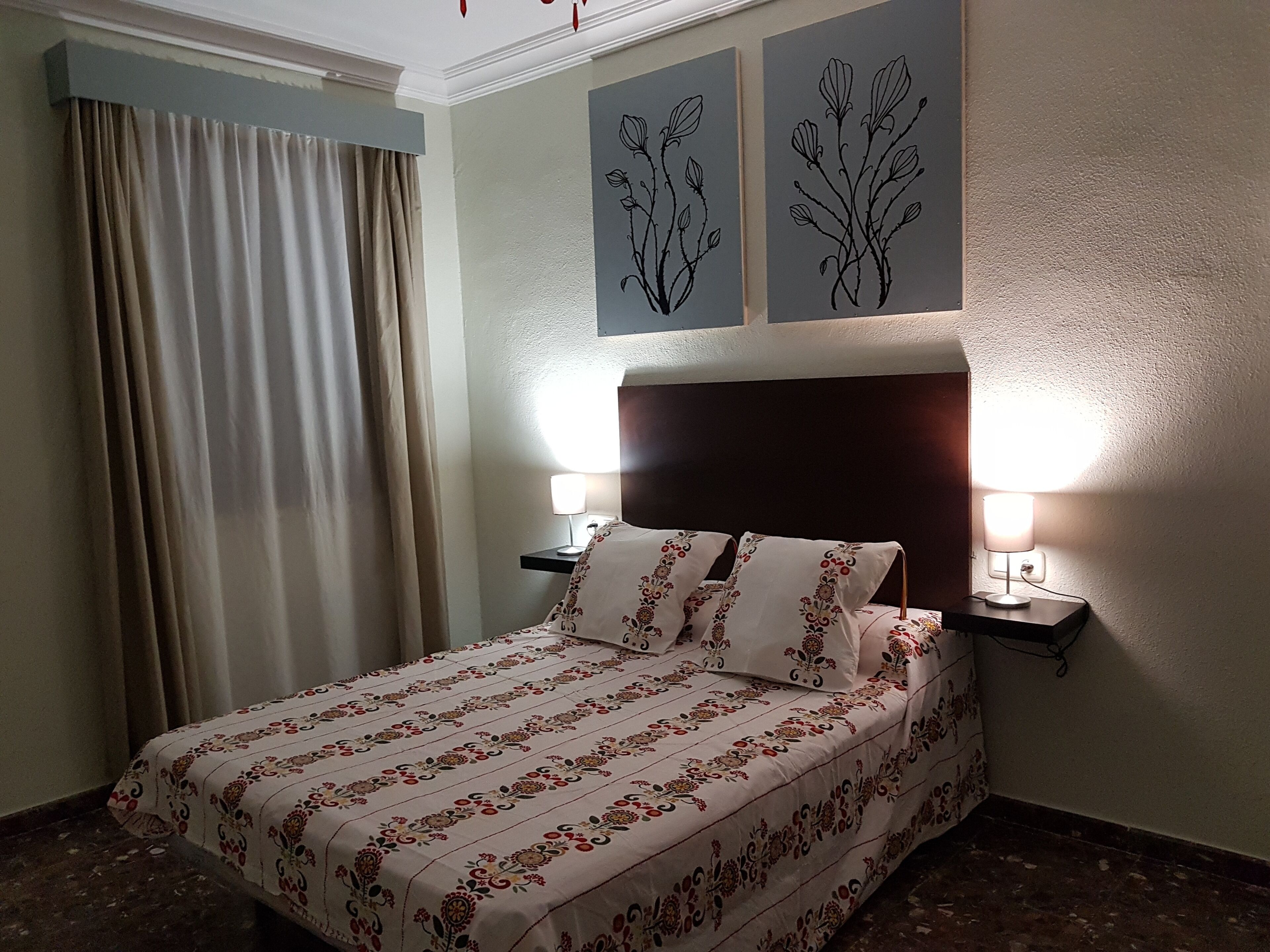 Una cama bien tendida con ropa de cama floral, dos lámparas de noche y una pared decorada con dos obras de arte botánicas.