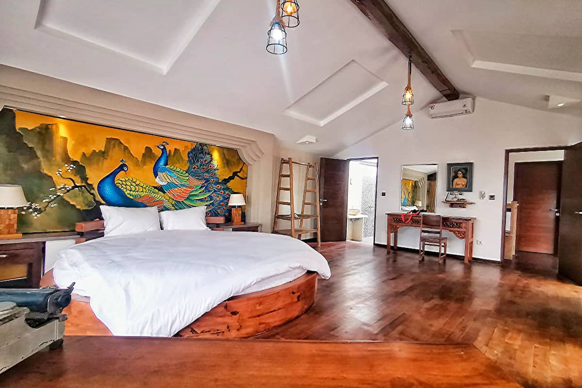A spacious bedroom with a large bed, wooden flooring, a peacock mural, and a desk with a chair.