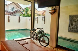 A room with a view of a swimming pool, a bicycle, and a mounted television. - Villa Himala Bali (Seminyak)