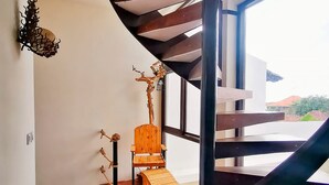 A modern interior with a wooden chair and a small table, a staircase, and a view through large windows. - Villa Himala Bali (Seminyak)
