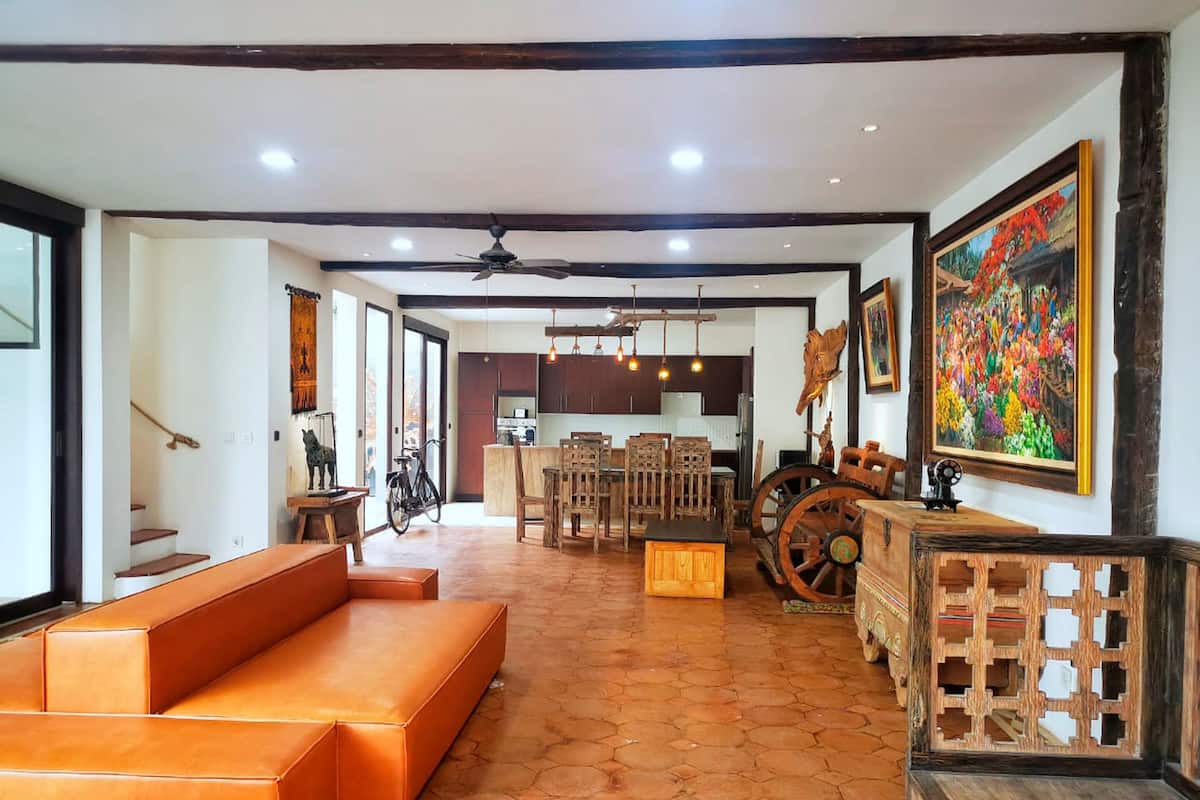 A spacious living area with a large sofa, wooden furniture, and a dining set.