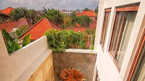 A narrow outdoor balcony with a small seating area, a decorative plant, and a view of neighboring buildings with red roofs. - Villa Himala Bali (Seminyak)