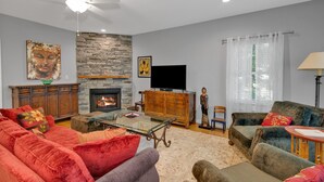 A living room with a stone fireplace, a television, and a ceiling fan. - The Hidden Gem | A Luxury Mountain Getaway (Weaverville)