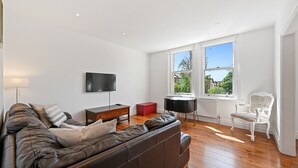 Un salon moderne avec un canapé en cuir, un téléviseur fixé au mur, une petite table et une fenêtre donnant sur l’extérieur.