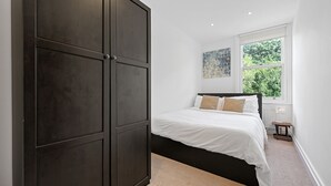 Une chambre avec une grande armoire sombre, un lit avec une literie blanche et une fenêtre donnant sur un paysage verdoyant.