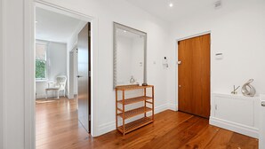 Un couloir avec un plancher en bois, une porte blanche, un miroir et une étagère en osier.