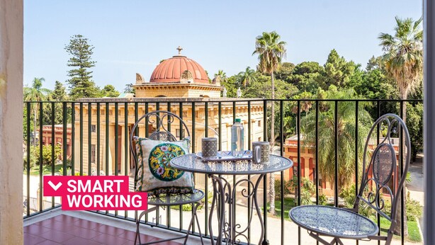 A balcony with a view of a historic building, a table with chairs, and a sign indicating smart working. - Un Balcone sull'Orto Botanico by Wonderful Italy (Palermo)
