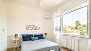A bedroom with a bed, two bedside tables, a window with a view of a building, and a radiator. - Un Balcone sull'Orto Botanico by Wonderful Italy (Palermo)