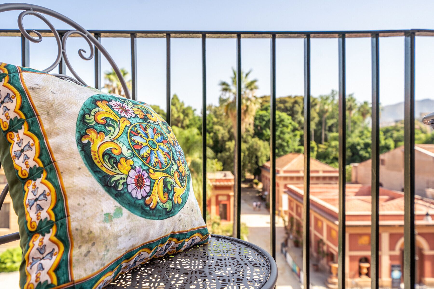 A balcony with a patterned cushion and a view of buildings and greenery.