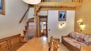 Una mesa de comedor de madera con sillas, un sofá de madera, una escalera y un cuadro en la pared.