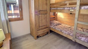 Una cama litera de madera con ropa de cama estampada, un armario de madera y una ventana con vistas a edificios.