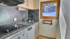 Una cocina compacta con un lavamanos, estufa y lavavajillas, una ventana con vistas a árboles, y un estante de madera.