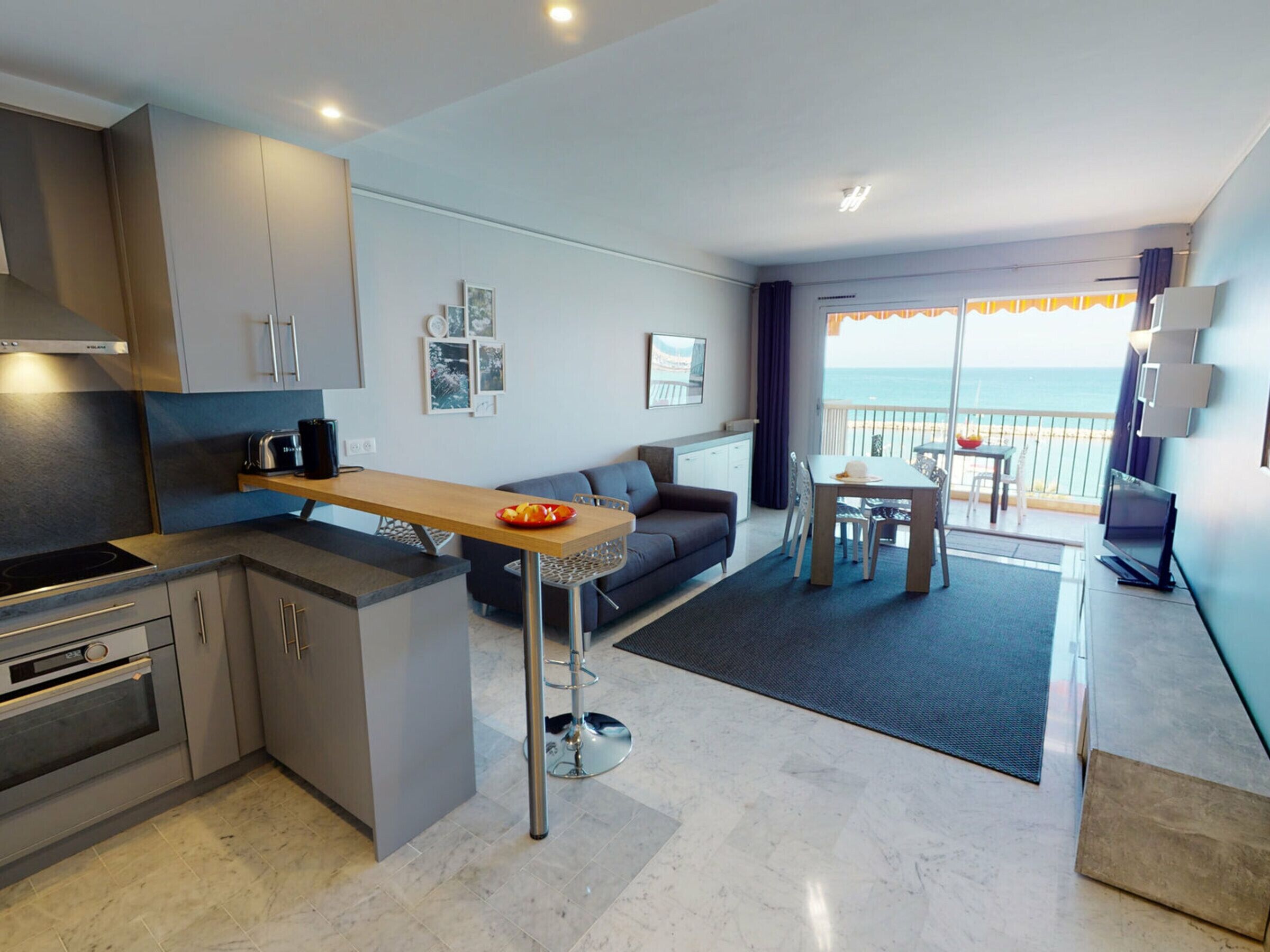 Cozinha moderna com área de refeições, um sofá e varanda com vista para o mar.