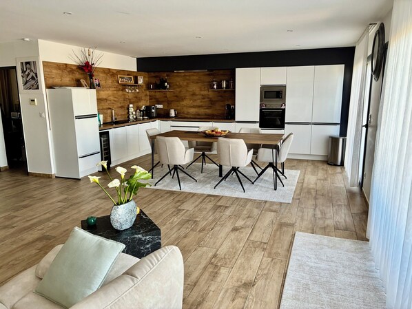 A modern kitchen with white cabinets, a wooden accent wall, and a dining area with a wooden table and chairs.
