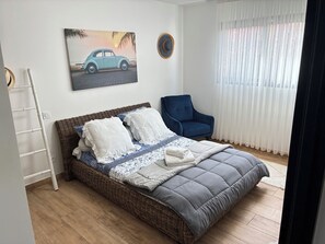 A bedroom with a bed, a chair, a painting, and a window with curtains.