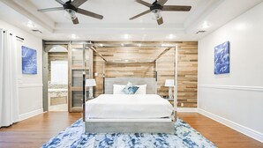 Ein Schlafzimmer mit hölzernem Kopfteil, einem Bett mit weißer Bettwäsche, zwei Nachttischlampen und einem Deckenventilator.