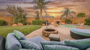 Ein Garten mit Pool, Feuerstelle, Gartenmöbeln und Blick auf den Sonnenuntergang.