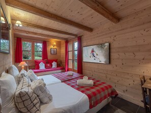 A wooden cabin room with two beds, red curtains, a painting, and a fireplace.
