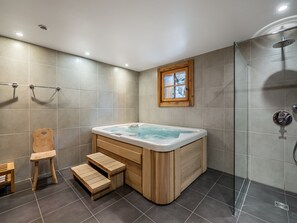 A modern bathroom with a wooden bathtub, a shower area, and a small wooden stool.