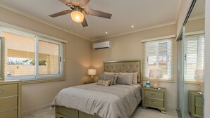 Une chambre à coucher avec un lit, des tables de chevet, un ventilateur de plafond et des fenêtres équipées de stores.