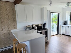 A modern kitchen with white cabinetry, a central island with stools, a stove, and a dishwasher.