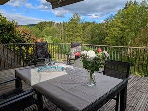 En terrasse med et bord, stole og en blomstervase.