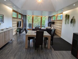 A modern kitchen with a dining area, wooden cabinets, and a large window offering a view of greenery.