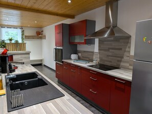 Een moderne keuken met rode kastjes, een roestvrijstalen afzuigkap en een zwart aanrecht.