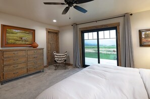 Un dormitorio con cama, cómoda de madera, silla, ventilador de techo y una ventana grande con vistas al exterior.