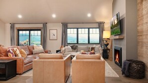 Uma sala de estar espaçosa com lareira, janelas amplas com vista e um espaço de estar aconchegante.
