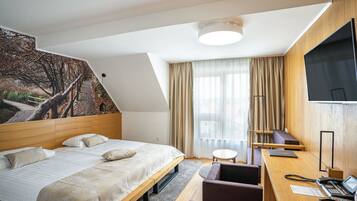 Habitación de hotel con cama, escritorio, silla, lámpara y una ventana grande con cortinas.