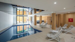 A modern indoor swimming pool with lounge chairs and wooden paneling. - Hotel Palcich (Rakovica)