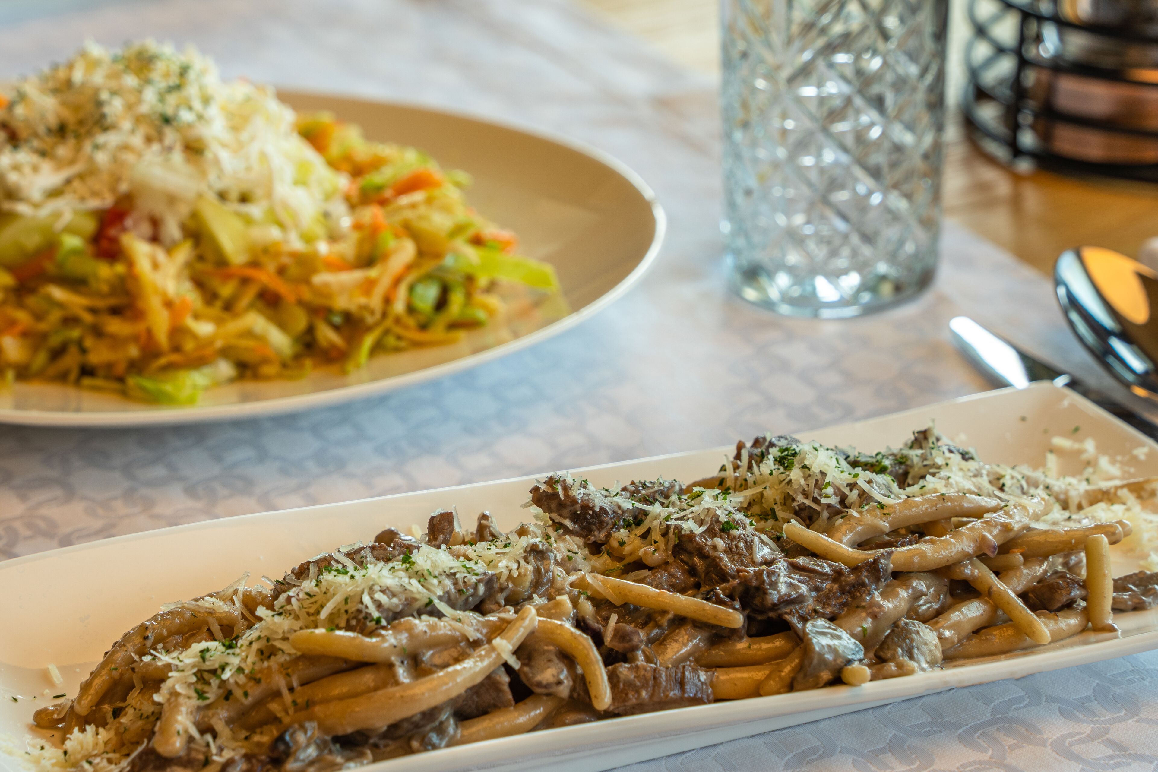 A dining table with two plates of pasta dishes.