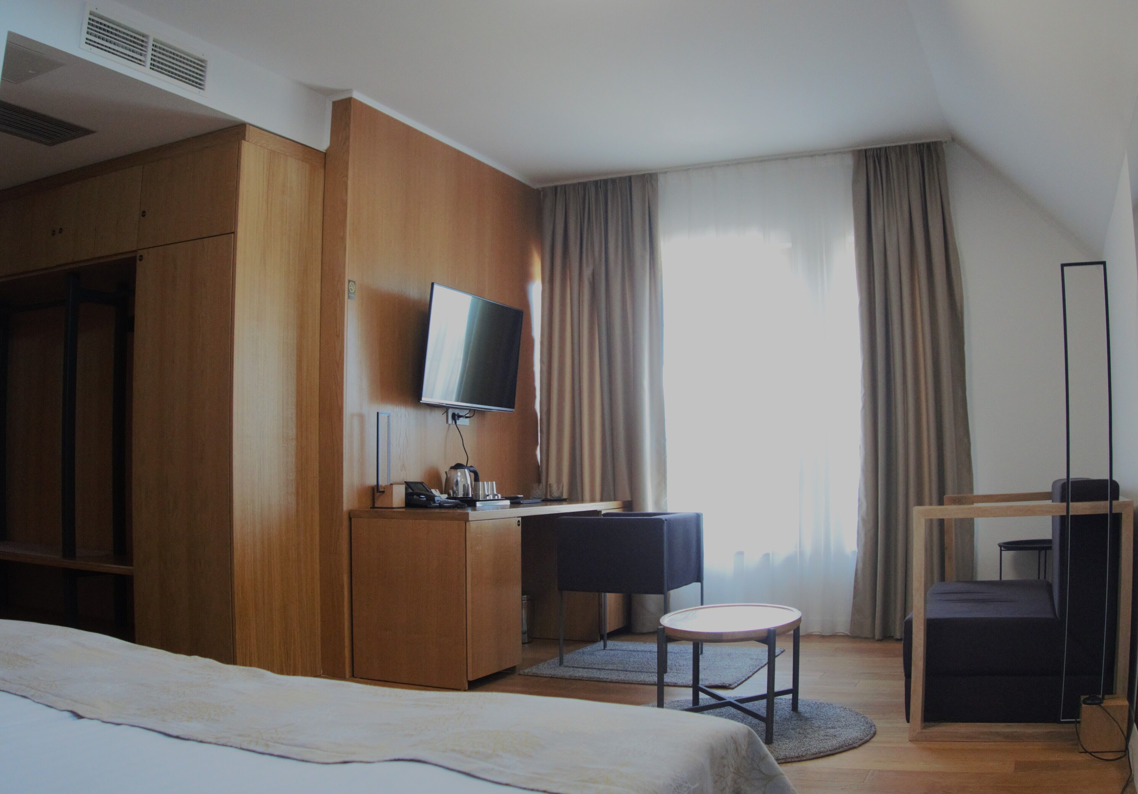 A hotel room with a bed, a desk with a chair, a television, and a wardrobe.