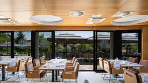 A restaurant with outdoor seating, wooden tables, and chairs, and large windows offering a view of the outdoor area. - Hotel Palcich (Rakovica)