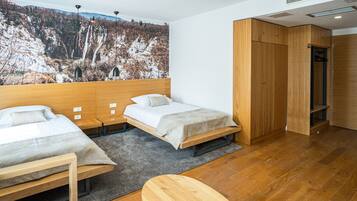 A modern hotel room with two beds, a wooden wardrobe, and a large wall mural of a mountainous landscape.